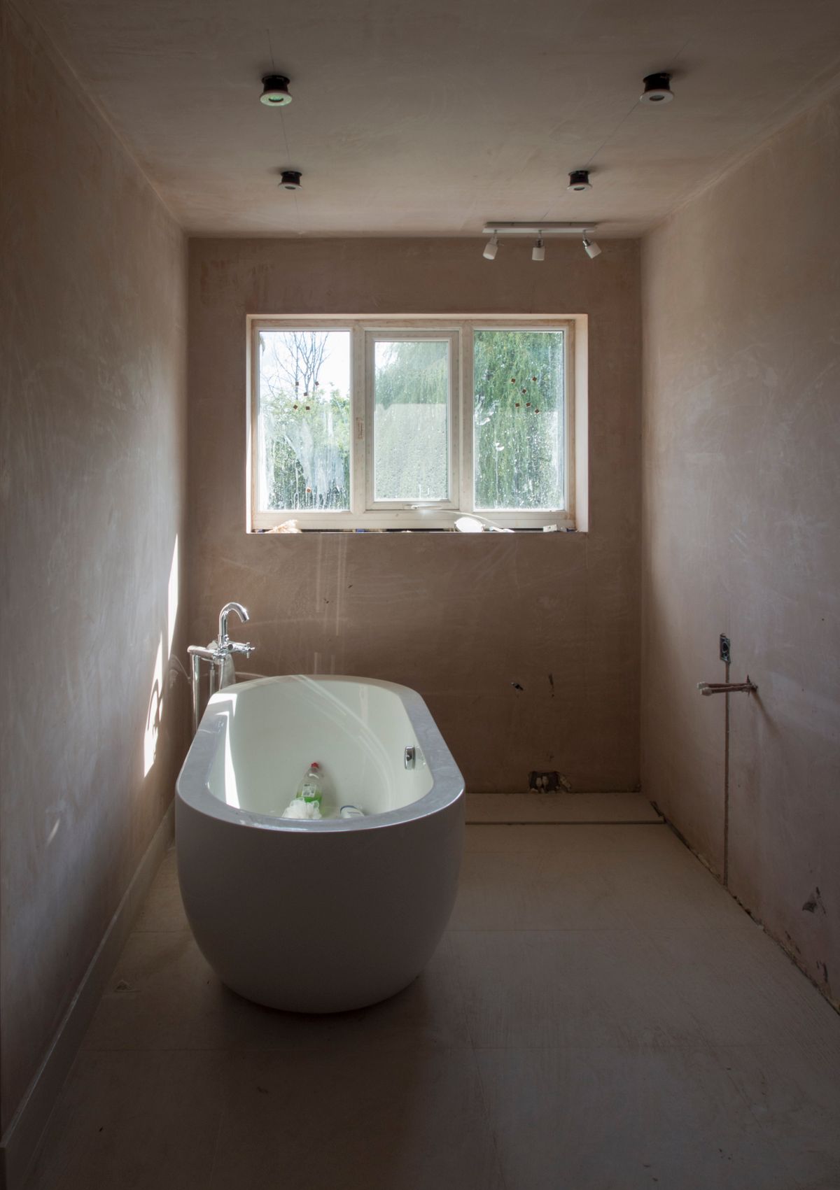 Bathroom mid-renovation with freshly plastered walls and a new freestanding bath