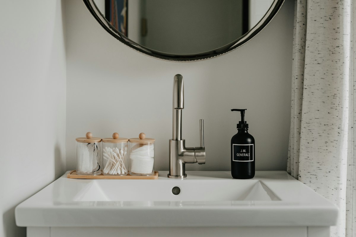 Clean bathroom basin with round mirror and soap dispensers